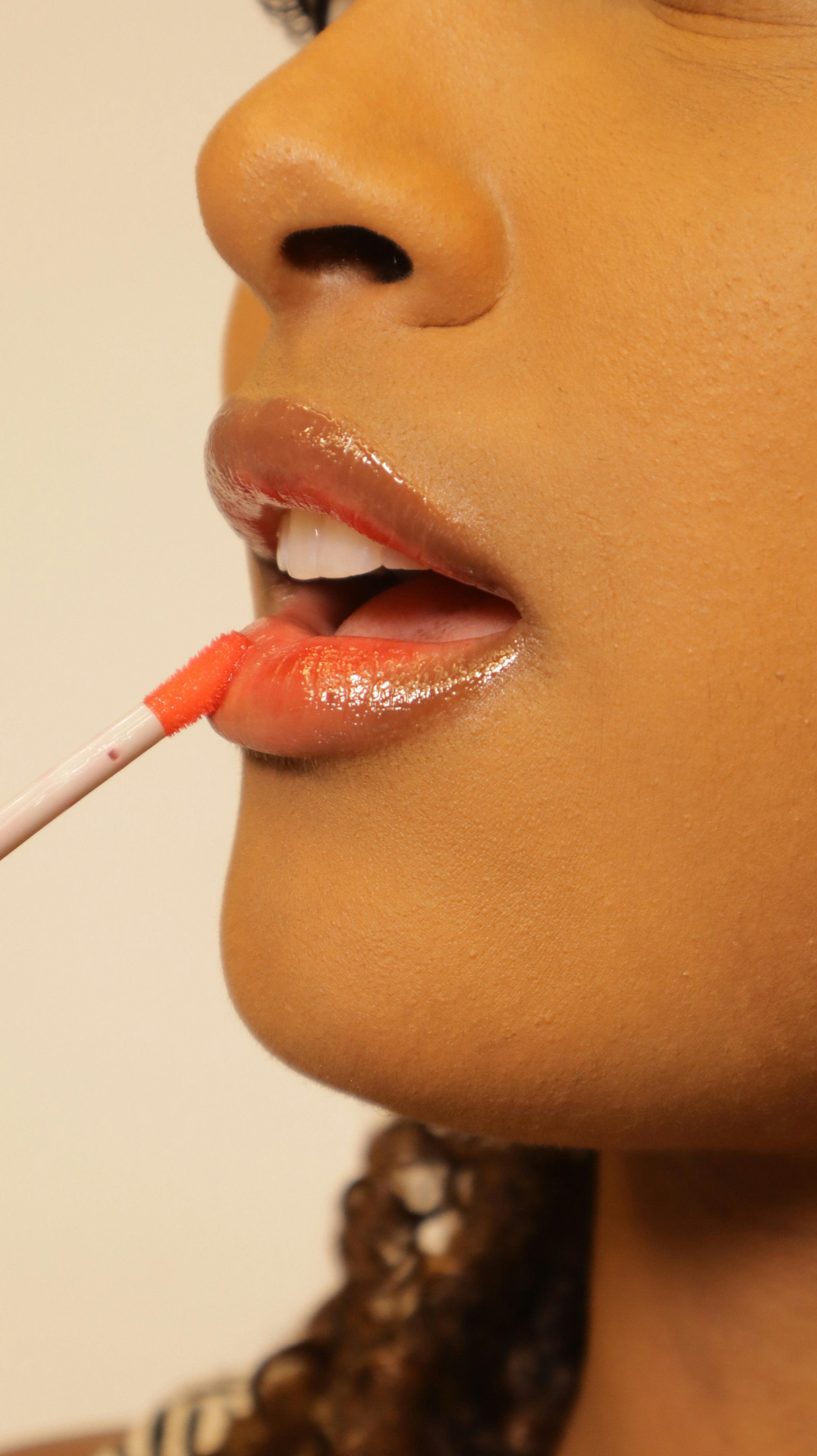Lips Gloss Side profile of a woman applying coral lip gloss enhances her lips, capturing a beauty routine.